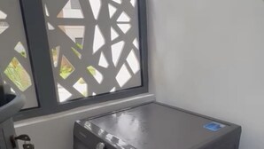 A compact, modern laundry room with a built-in washer and dryer, a window with a decorative screen, and a visible electrical outlet. - 2 Bed Apartment - Balcony, Parking, Wifi (Casablanca)