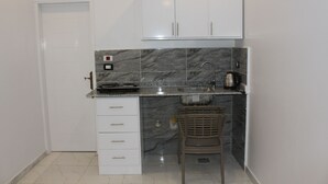Una cocina compacta con armarios blancos, salpicadero de mármol, un lavabo y una silla de mimbre.
