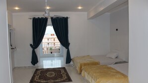 Una habitación con dos camas, ventilador de techo, ventana con cortinas y vista a edificios.