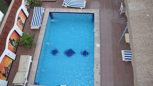 Una piscina rectangular con borde de azulejos, rodeada de sillas de descanso y sombrillas.