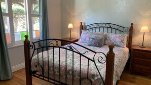 A bedroom with a metal bed frame, floral bedding, two bedside tables with lamps, a window with curtains, and a patterned wall. - Florence Cottage, 10 minutes from Hunter Valley Vineyards. Family friendly.  (Cessnock)
