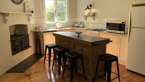 A kitchen with wooden cabinets, a central island with stools, a built-in stove, a microwave, and a large clock on the wall. - Florence Cottage, 10 minutes from Hunter Valley Vineyards. Family friendly.  (Cessnock)