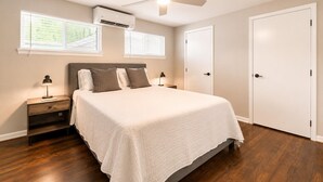 Une chambre à coucher comprenant un lit, des tables de chevet, un ventilateur de plafond, un appareil de climatisation et une porte.