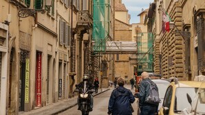 A narrow street with historic buildings, a tower, and a motorcyclist.
