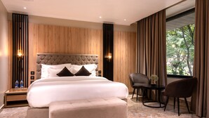 A modern hotel room with a large bed, a sitting area with a table and chairs, and a window with curtains. - Alpine hotel and villas (Dharamshala)