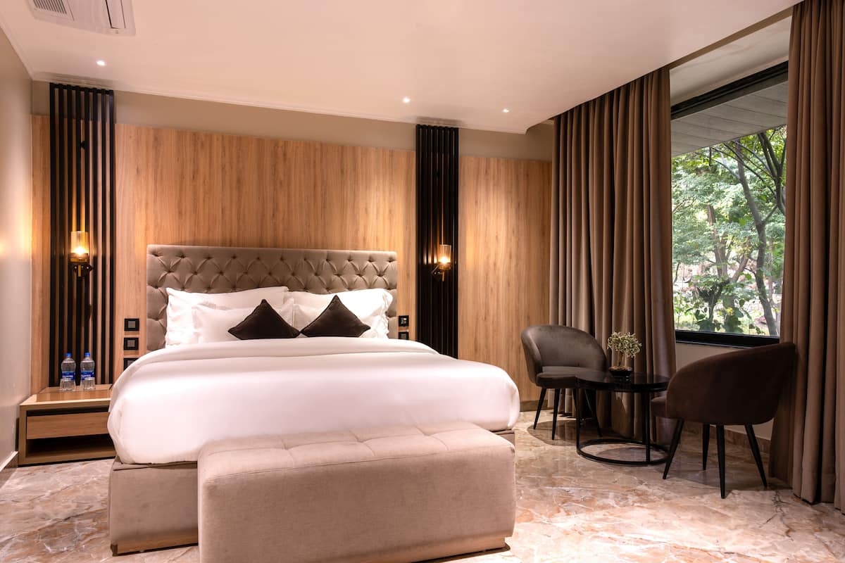 A modern hotel room with a large bed, a sitting area with a table and chairs, and a window with curtains.