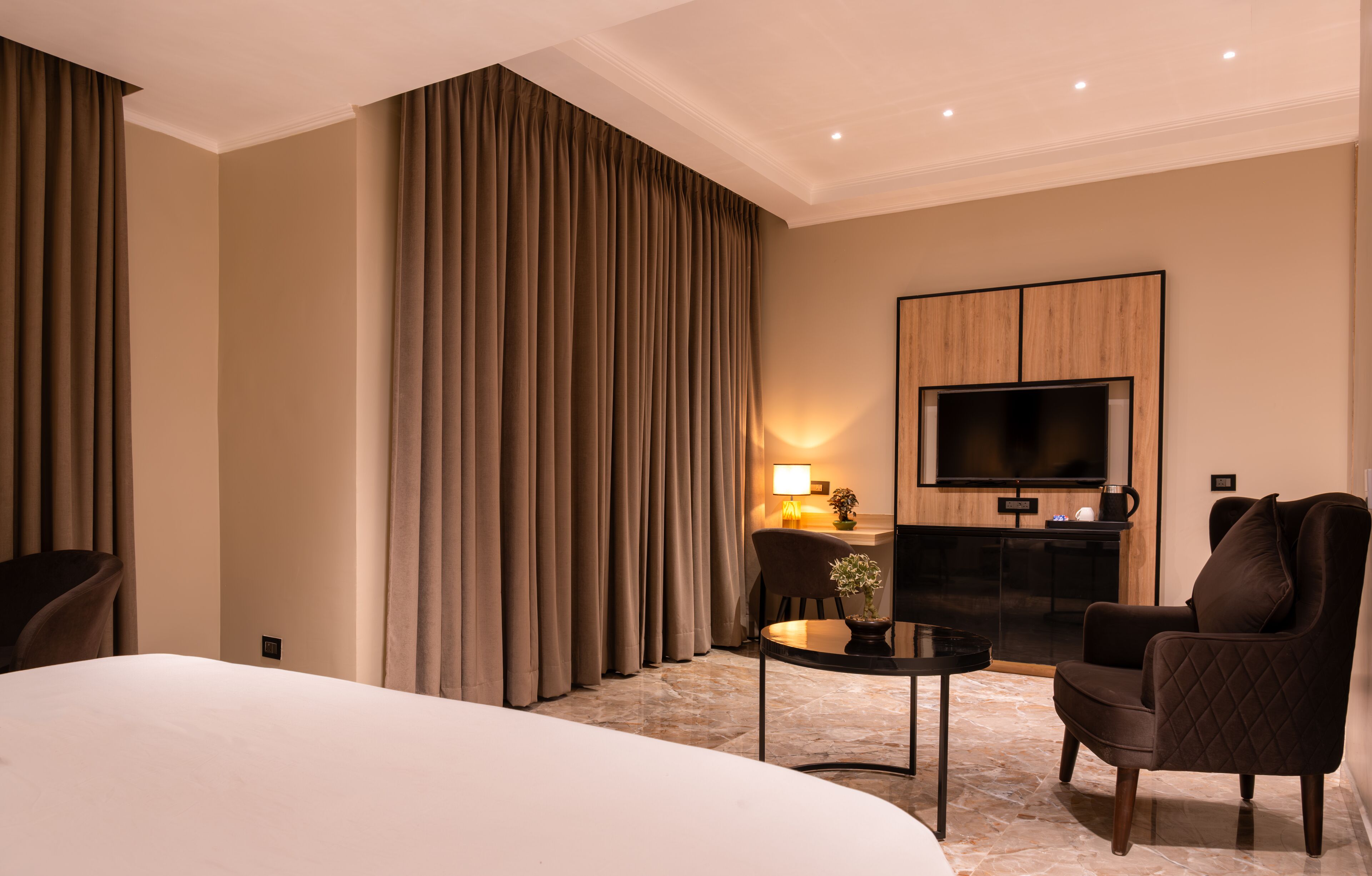 Una habitación de hotel con una cama grande, una zona de estar con una mesa y sillas, un televisor de pantalla plana y un minibar.