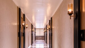A long, well-lit hallway with a polished floor, flanked by walls with light fixtures and doors on both sides. - Alpine hotel and villas (Dharamshala)