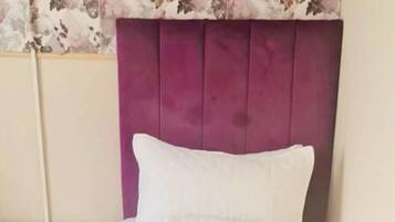 A bed with a purple headboard, white bedding, and a floral-patterned curtain.