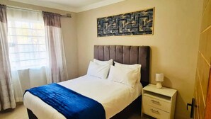 Habitación de hotel con cama, mesita de noche, lámpara y ventana con cortinas.