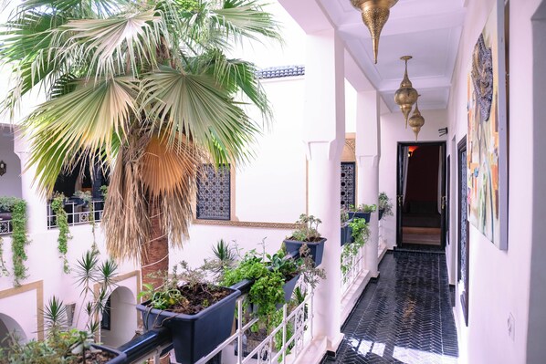 A corridor with potted plants, a palm tree, and hanging lanterns. - Riad Oasissime Marrakech (Marrakech)
