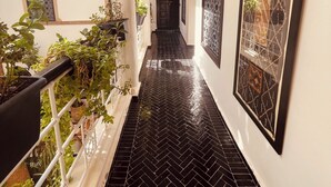 A corridor with black herringbone tiles, potted plants, and framed artwork on the walls. - Riad Oasissime Marrakech (Marrakech)