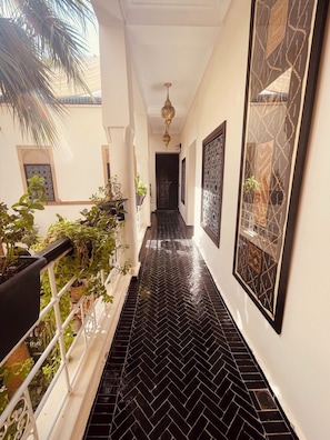 A corridor with black herringbone tiles, potted plants, and framed artwork on the walls. - Riad Oasissime Marrakech (Marrakech)