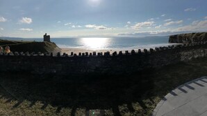 Una fortificación costera con un muro de piedra y una torre de vigilancia, dominando el mar.