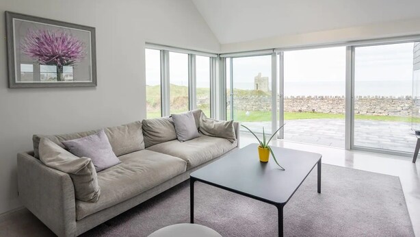 Una sala de estar moderna con un sofá color crema, una mesa de centro de vidrio y un ventanal con vistas a un castillo y el paisaje.