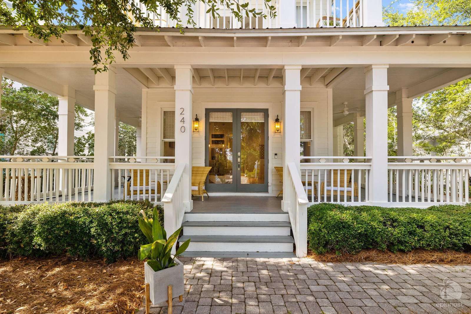 A white colonial-style building with a covered porch, numbered 240, and a small garden area with a potted plant.