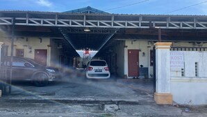 A car wash facility with a covered entrance, a sign indicating a cost for services, and a visible car in the process of being washed. - OYO 93178 Al Bait Homestay. (Lhokseumawe)