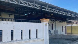 A building with a metal roof structure, a white wall with several windows, and a visible door. - OYO 93178 Al Bait Homestay. (Lhokseumawe)