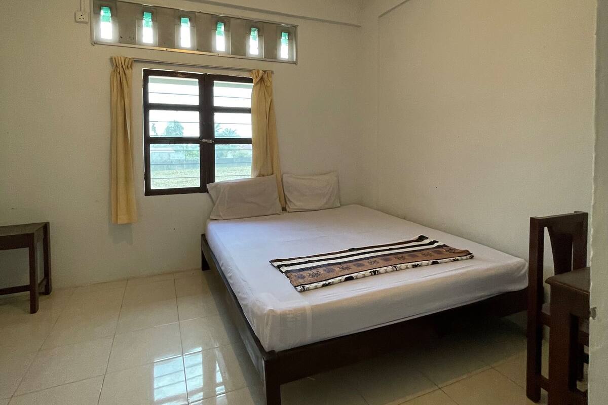 Une chambre à coucher avec un lit, une fenêtre avec des rideaux, une table de chevet et une chaise.
