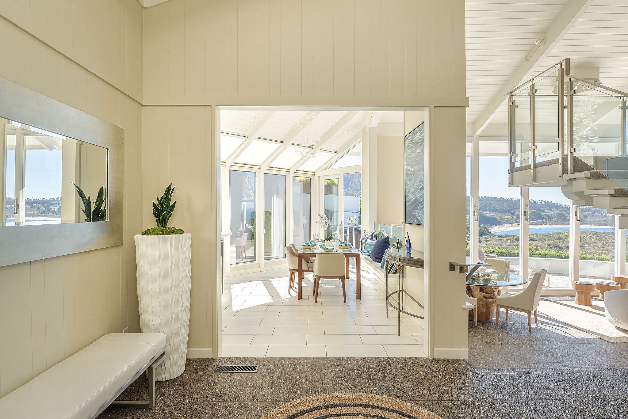 Una habitación amplia con un ventanal grande, un banco, una zona de comedor con sillas y vistas al exterior.