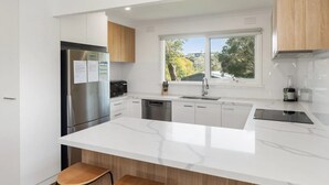A modern kitchen with a large island, stainless steel appliances, and a view of trees outside.