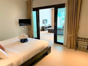 A hotel room with a bed, a TV mounted on the wall, a desk with a chair, and a sliding glass door leading to an outdoor area. - Olive 2 Beds Beachfront Condo Resort (Rawai)