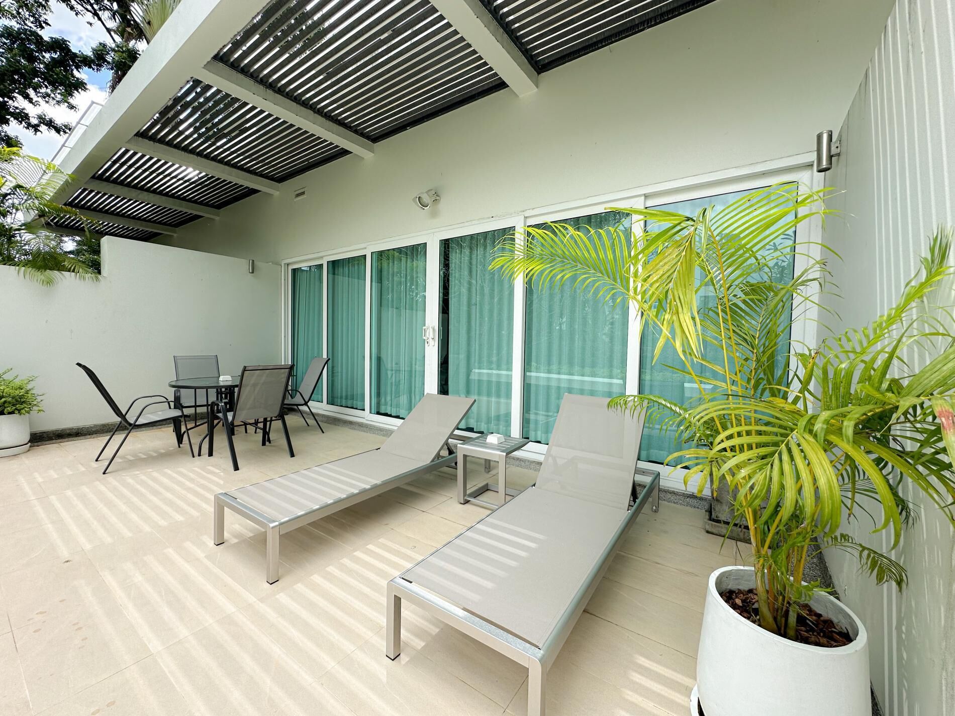 A modern outdoor patio with a dining area, lounge chairs, and potted plants.
