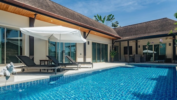 Ein Swimmingpool mit Liegestühlen und Sonnenschirmen, umgeben von moderner Architektur und großen Fenstern.