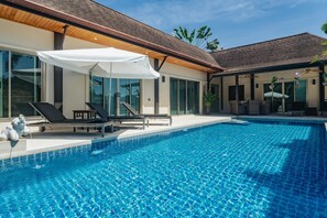 A swimming pool with lounge chairs and umbrellas, surrounded by modern architecture and large windows. - Ivory Pool Villa, Dreamy Villa With Sparkling Pool (Tambon Rawai)