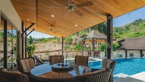 Ein überdachter Außenbereich mit Pool, Korbmöbeln und Deckenventilatoren.
