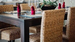 Ein Essbereich mit einem dunklen Holztisch, Korbstühlen und einer zentral platzierten Vase mit weißen Blumen.