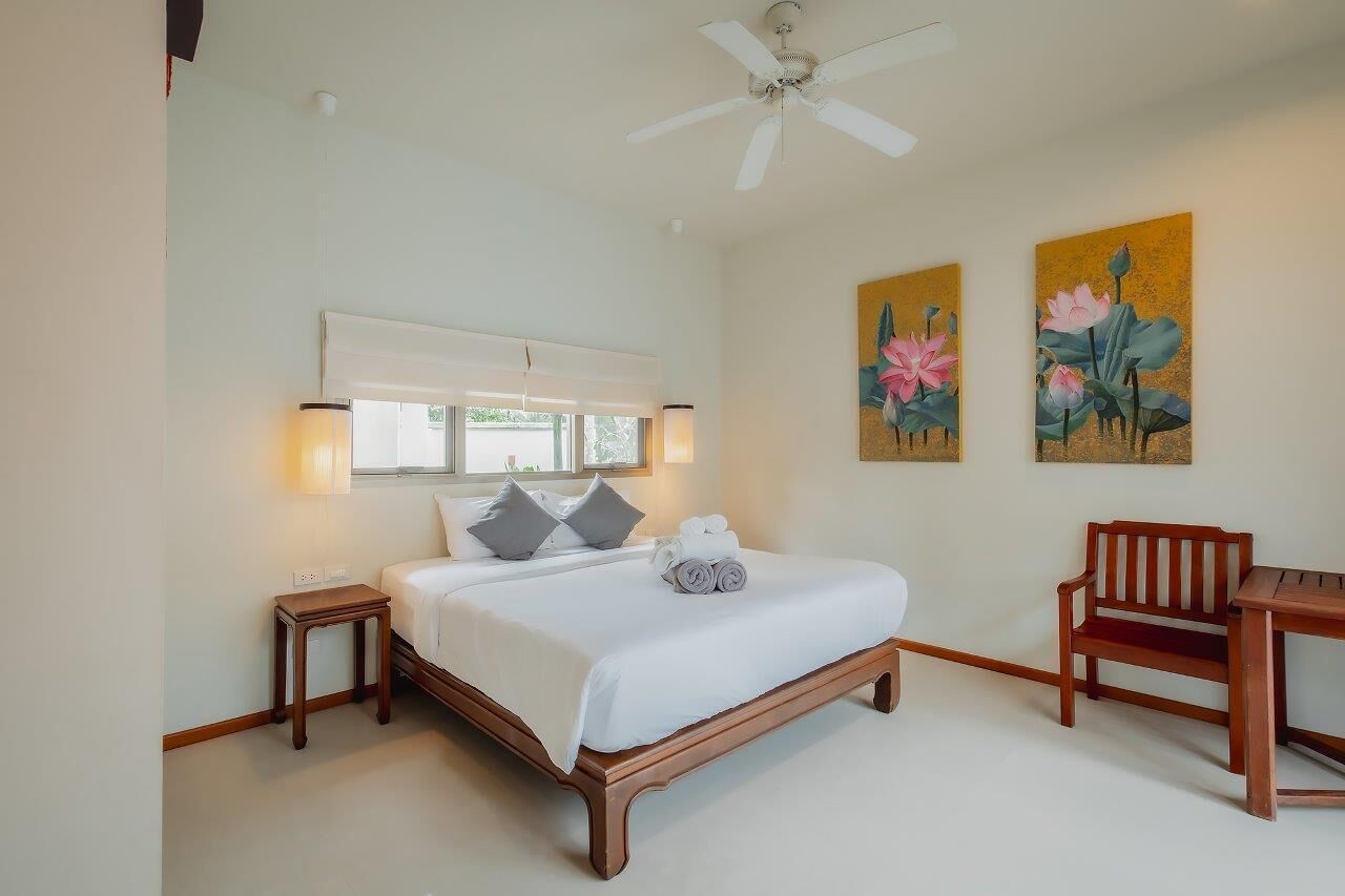 A bedroom with a bed, bedside tables, a ceiling fan, a window, and artwork on the walls.