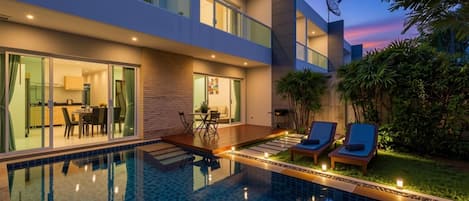 Una casa moderna con piscina, comedor y sala de estar con sillones.