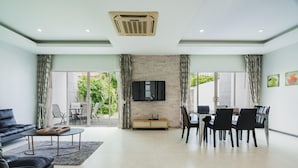 A modern living room with a sofa, coffee table, TV, and dining area with chairs. - Trixie Town House 2 With Private Pool (Rawai)