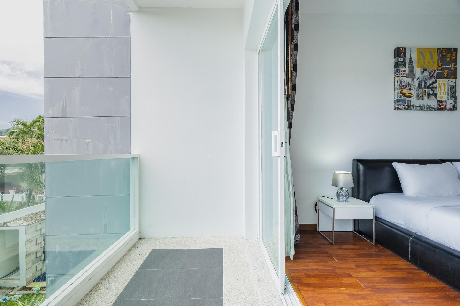 A balcony with a glass door, a bed with a nightstand, and a wall with a cityscape poster.