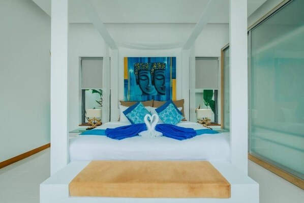 A modern hotel room with a large bed, a blue artwork above the bed, and a view of the sea through the window.