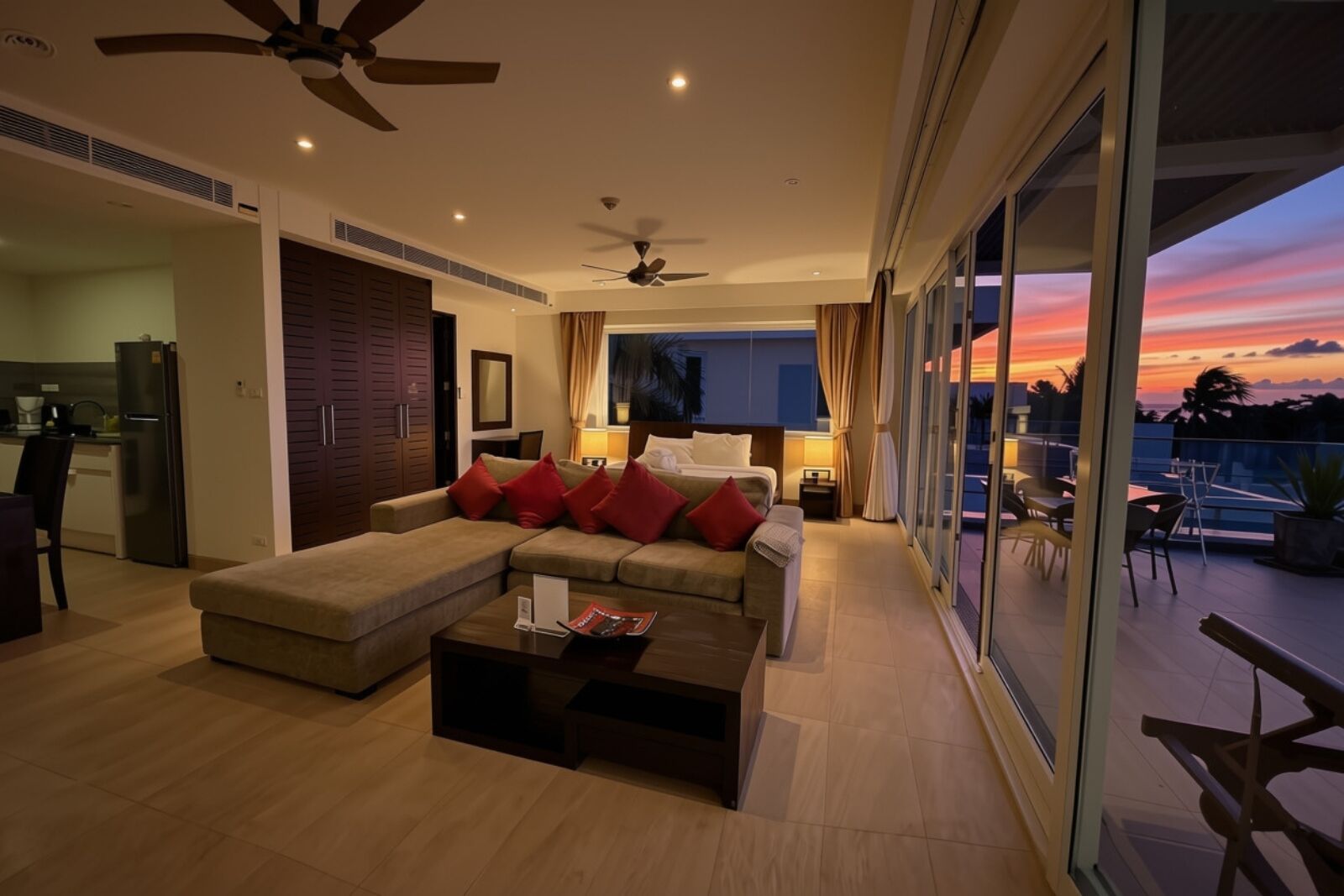 A modern living room with a sectional sofa, a coffee table, and a view of the sunset through large windows.