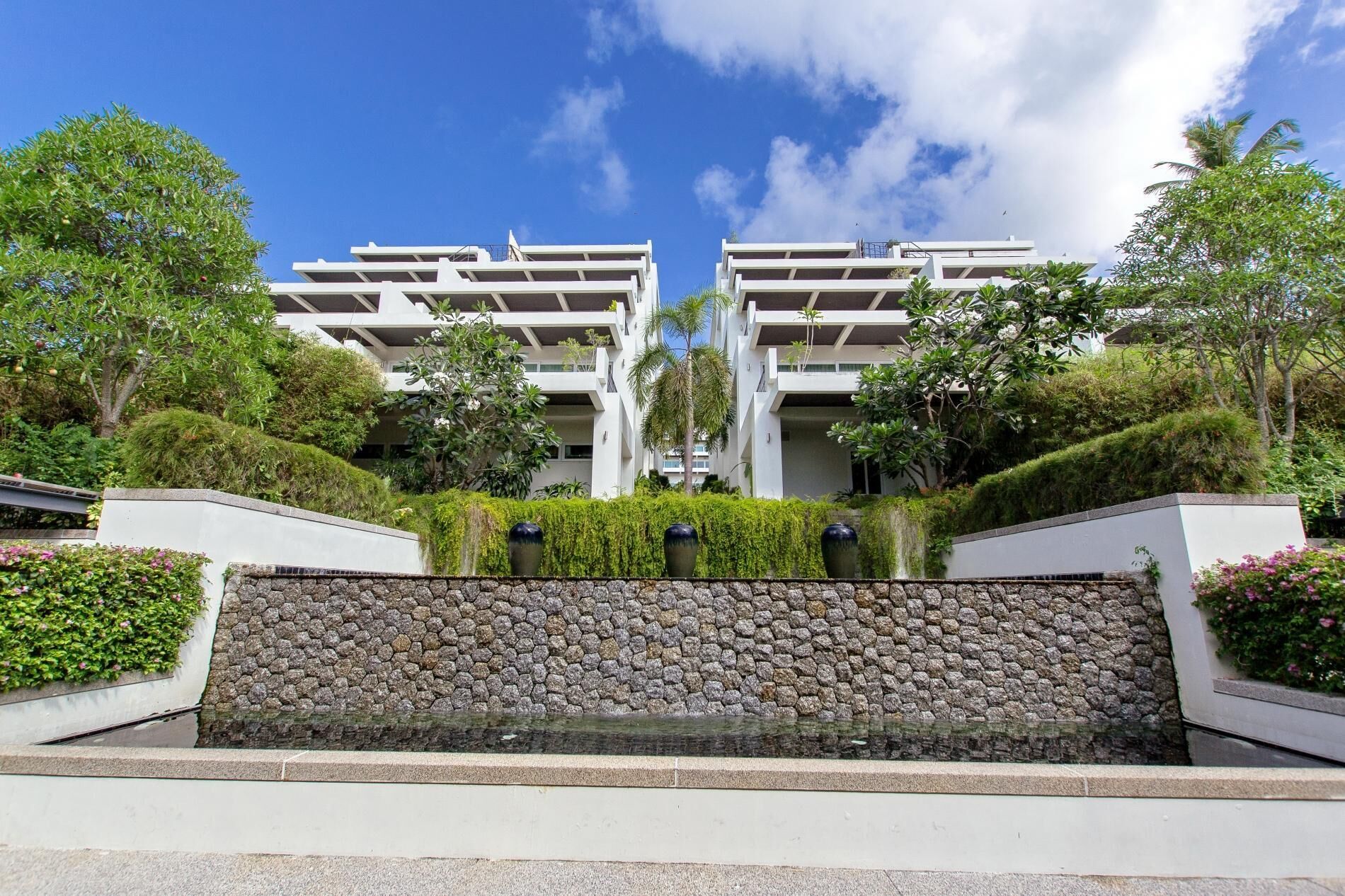 A modern building with a symmetrical design, featuring a central water feature and lush greenery.