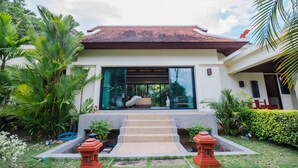 Une maison moderne dotée d’une grande porte vitrée, entourée d’une végétation luxuriante et d’un jardin bien entretenu.