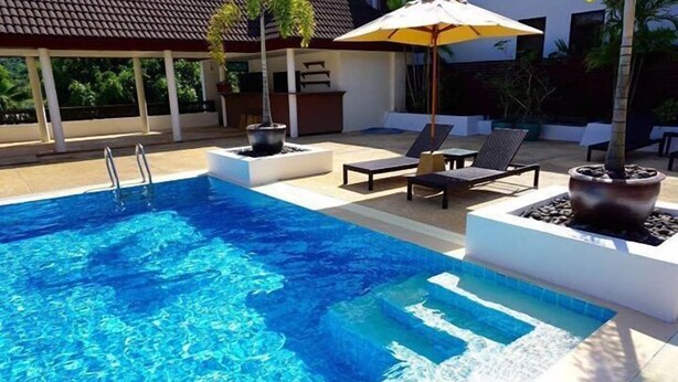 Een zwembad met helderblauw water, omringd door ligbedden en een overdekt gebied met parasols.