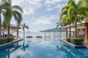 A pool area with lounge chairs and umbrellas, surrounded by palm trees and a view of the sea. - Poppy Beachfront Residence (Rawai)