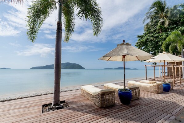 A wooden deck with lounge chairs and umbrellas overlooking a calm sea with distant islands. - Poppy Beachfront Residence (Rawai)