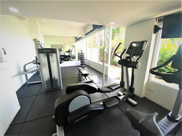 A gym with cardio machines, weight equipment, and a large window providing natural light.