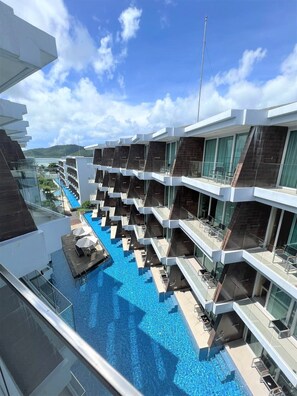 A modern hotel with multiple balconies, a central swimming pool, and a view of the sea.