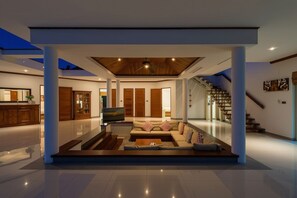 Una sala de estar moderna con un televisor de pantalla plana, un sofá y una mesa de centro. Se ve una escalera con barandillas de madera que conduce a otro nivel.