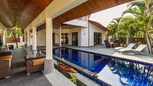 Ein Poolbereich mit Liegestühlen, einer Holzbalkendecke und tropischen Pflanzen.