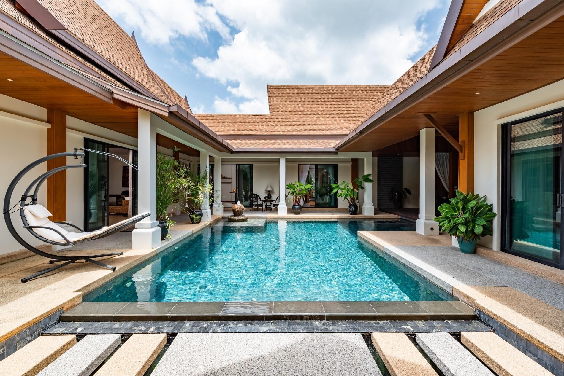 A modern pool area with a clear blue pool, surrounded by wooden pillars and potted plants.