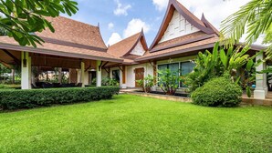 Um edifício em estilo tradicional com um alpendre coberto, gramado exuberante e plantas tropicais.