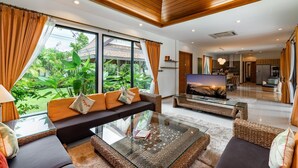 Sala de estar moderna com televisão grande, assentos confortáveis e vista para vegetação exuberante.