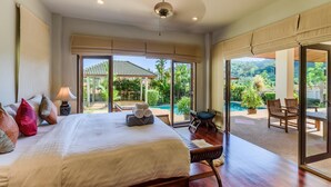 Une chambre spacieuse avec un grand lit, une vue sur la piscine et le jardin, et un balcon équipé de chaises.